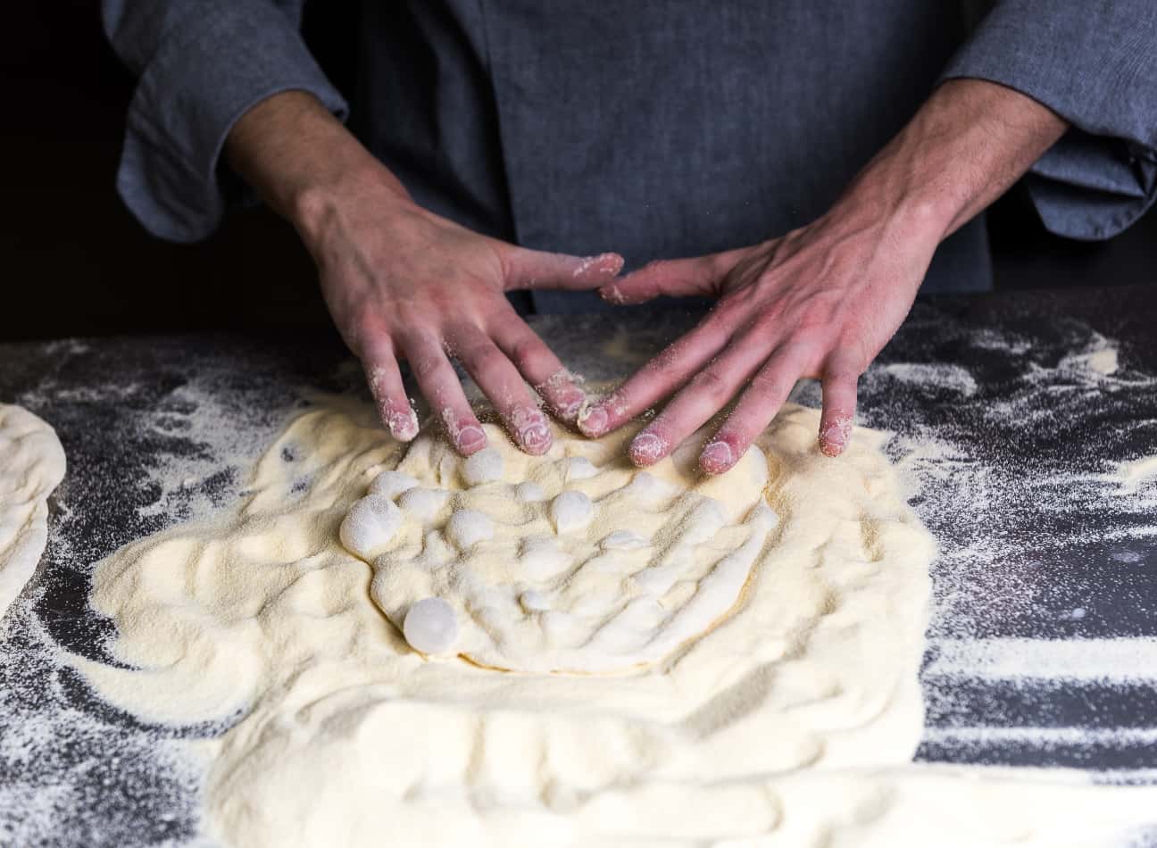 Dettagli delle mani di un cuoco che impastano una Pinsa.