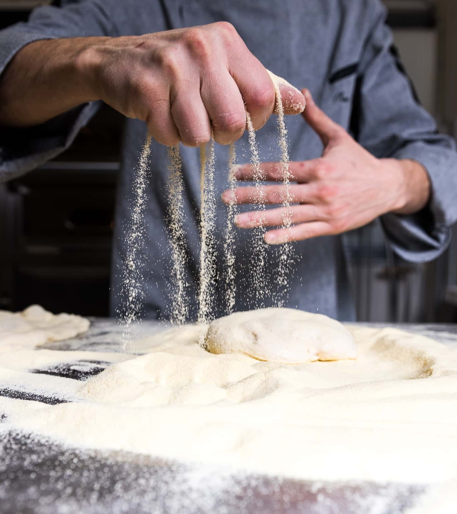 Detail of a cook's hand spreading flour while preparing a Pinsa.
