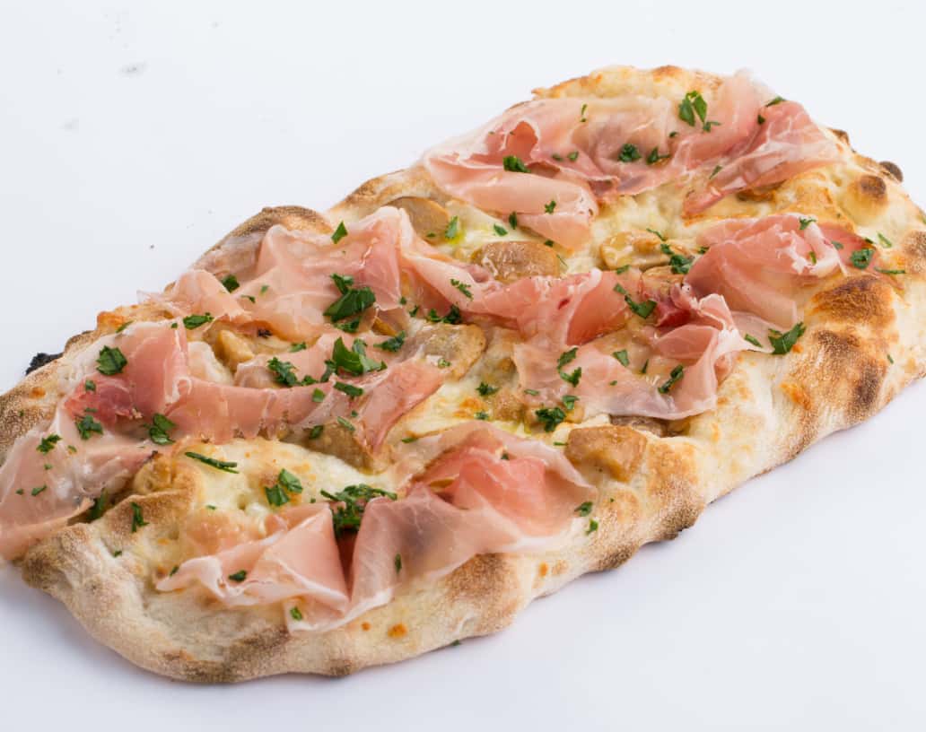 Photo of a Pinsa topped with prosciutto and parsley.