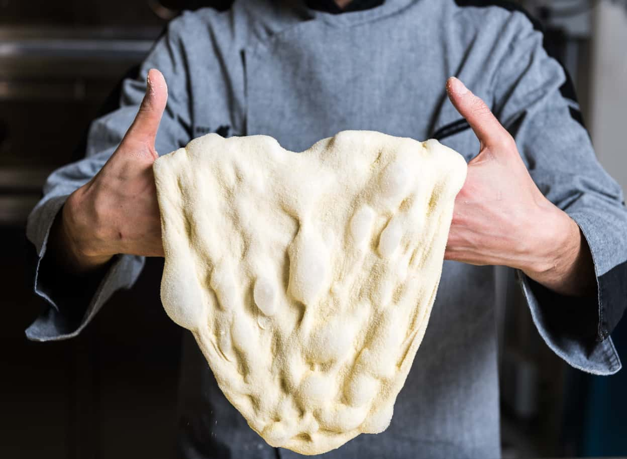 Foto delle mani di un cuoco che sorreggono un impasto di Pinsa.