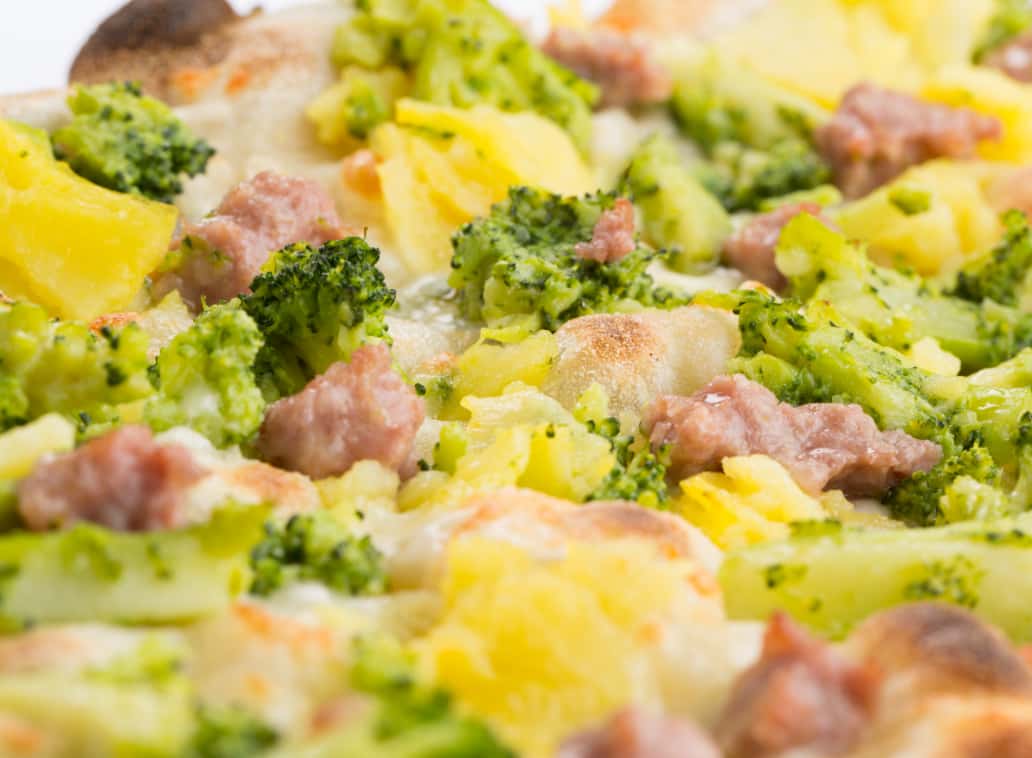 Detail of a Pinsa topped with sausage, broccoli and potatoes