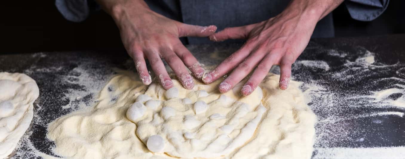 Dettaglio delle mani di un cuoco che prepara la Pinsa.