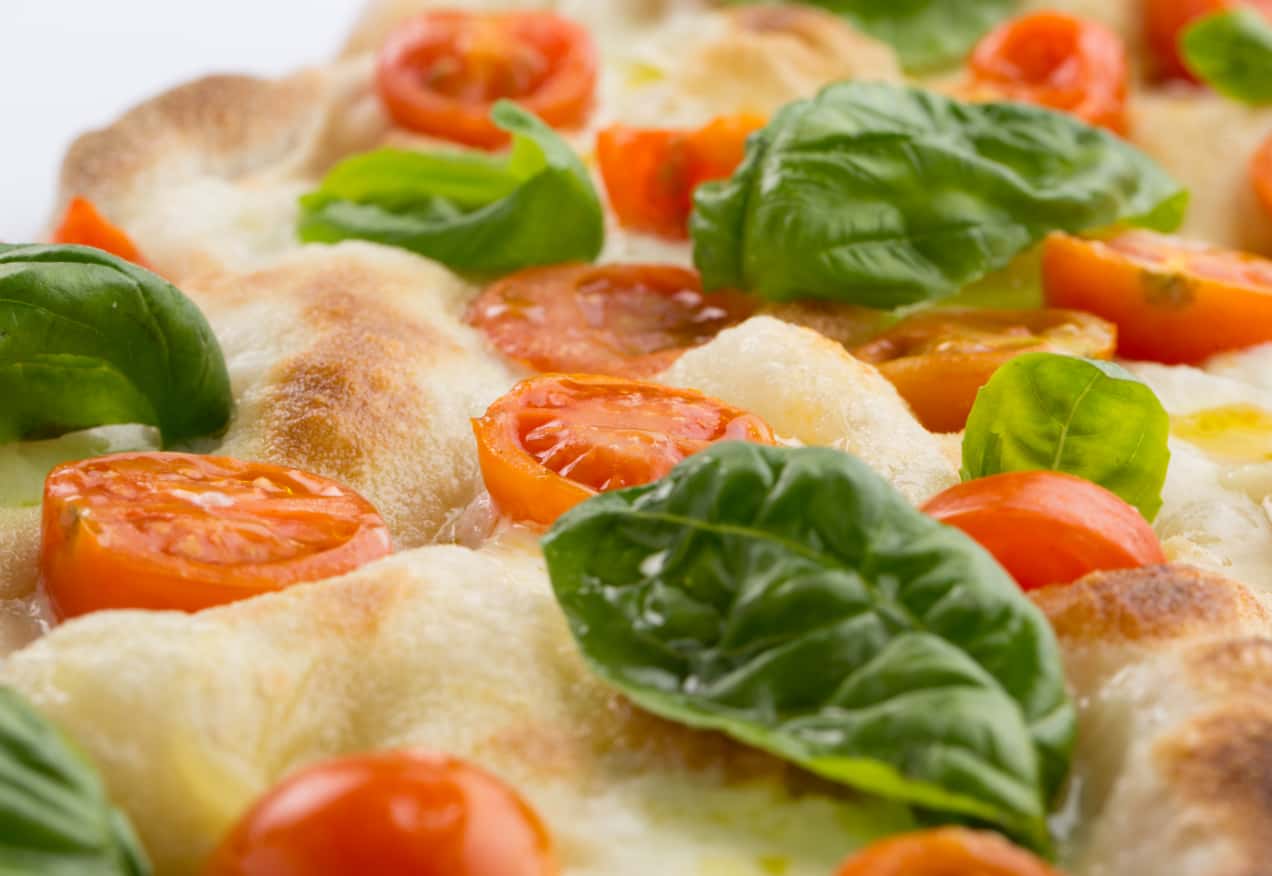 Detail of a Pinsa topped with cherry tomatoes and basil