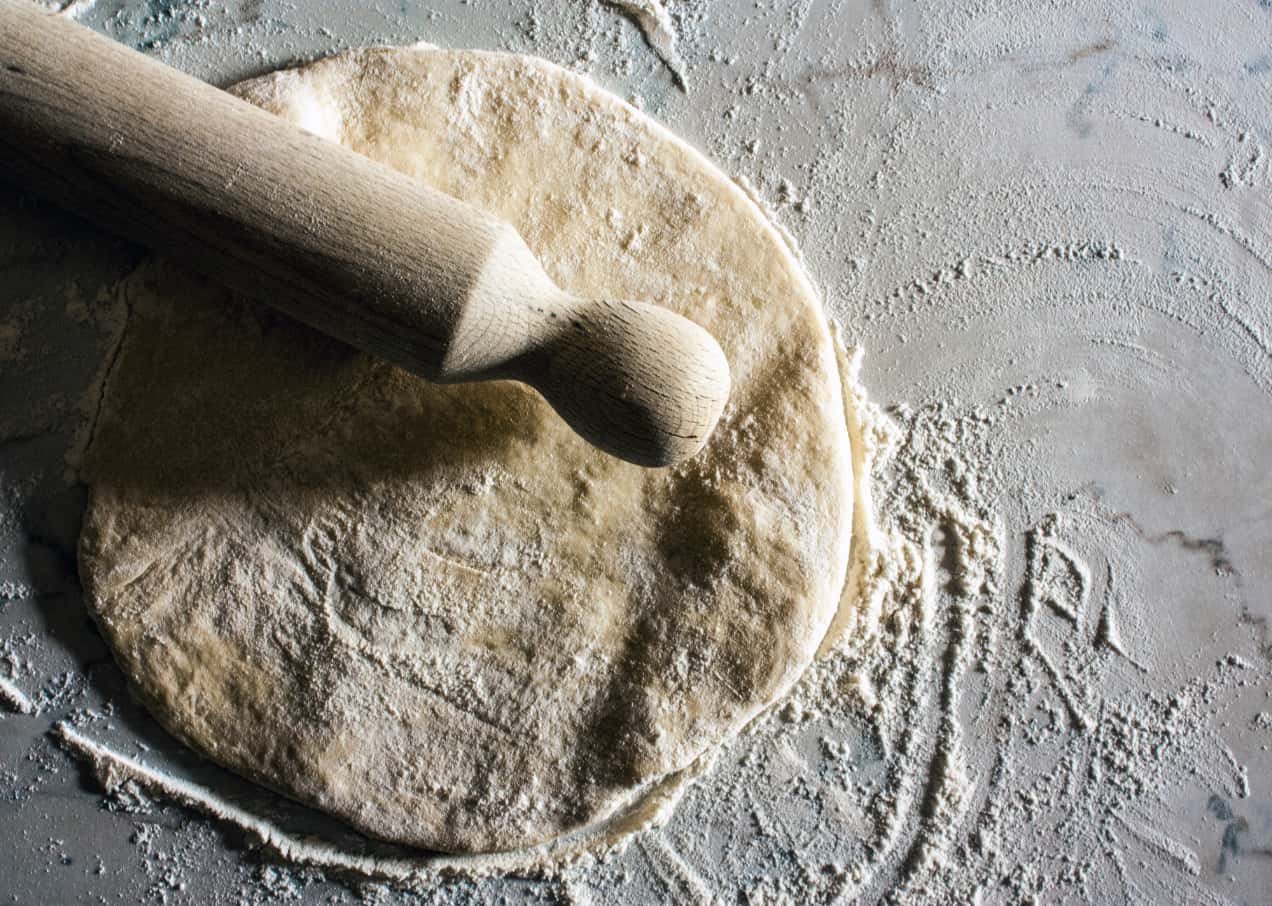 Photo of a rolling pin and dough with flour around them.