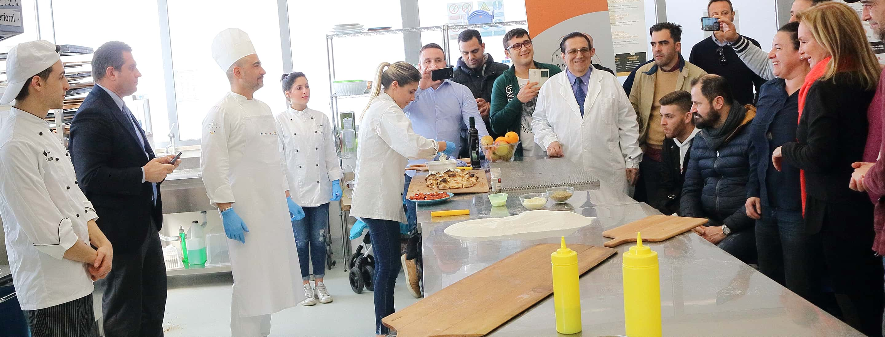 Foto di Corrado Di Marco insieme a due cuochi e gli spettatori di una dimostrazione di Pinsa Romana