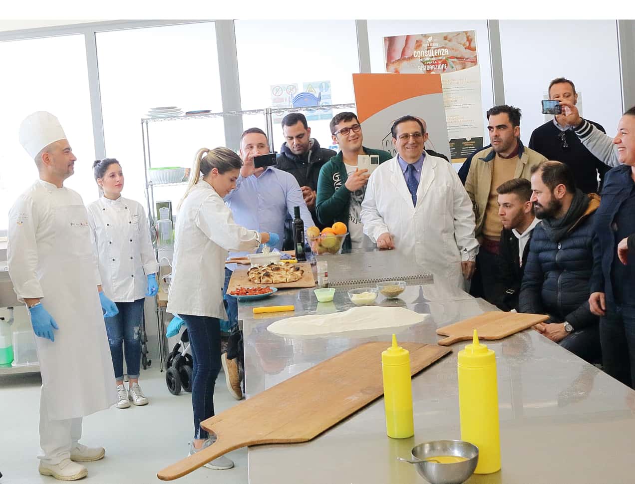 Photo of Corrado Di Marco together with two chefs and spectators at a Pinsa Romana demonstration